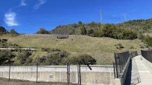 Photo simulation of wildlife undercrossing. Photo taken from a trail below, looking up at a hill. There is a large opening below the highway.