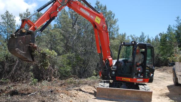 Man uses excavator to dig up nonnative vegetation to create a fuel break